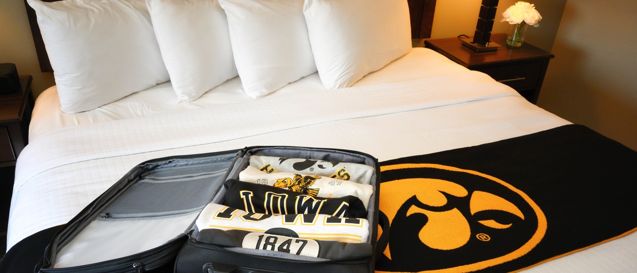 Open luggage container with Iowa Hawkeye t-shirts sitting on a hotel bed